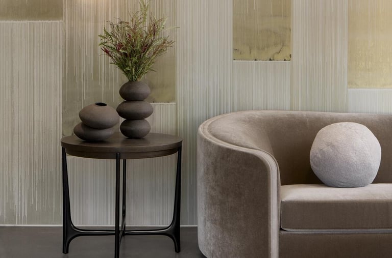 Modern living room featuring a velvet sofa, marble side table with ceramic vases, and textured wallpaper.