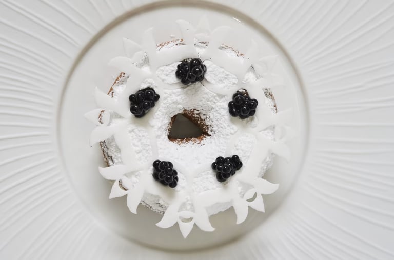 Powdered sugar dessert topped with blackberries and white chocolate curls.