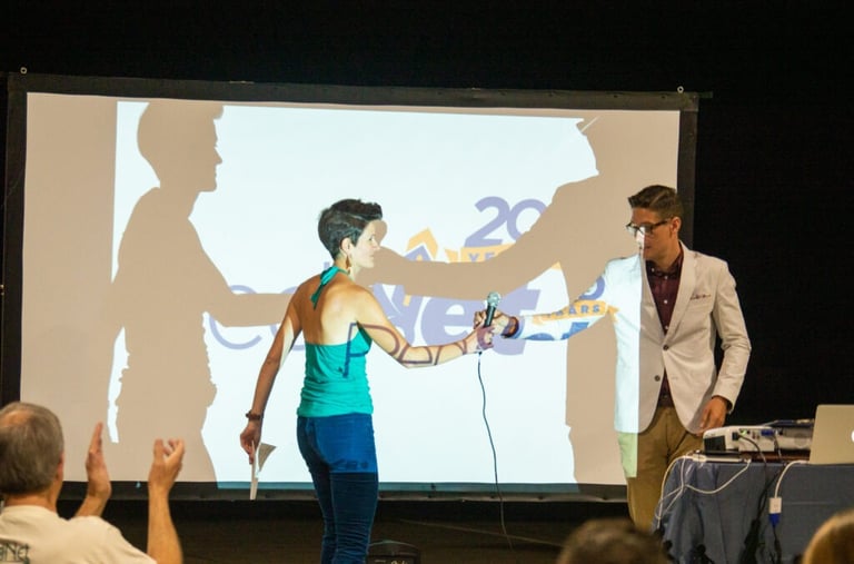 Two people exchanging a microphone in front of a screen