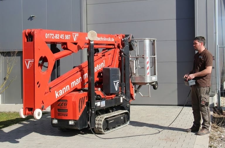 Schreinermeister Ferdinand Volk steuert die rote Raupen-Arbeitsbühne per Kabelfernbedienung vor seiner Werkhalle am Ammersee.