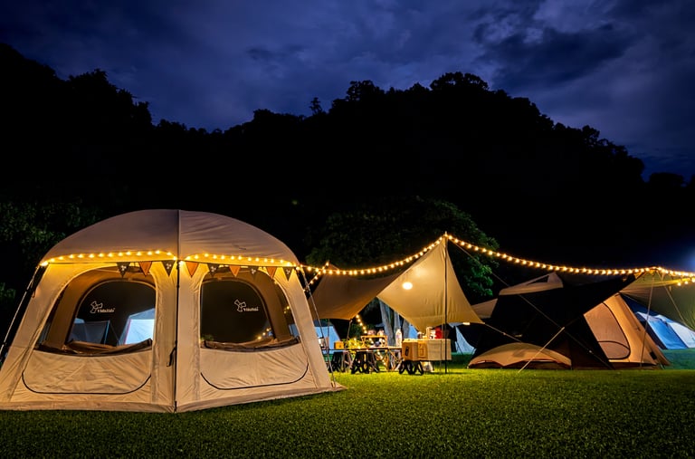 Illuminated camping tents and string lights on a grassy field at night with mountain silhouettes.