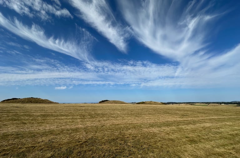 Dramatic clouds sweep up over a deep blue sky above a hilltop in the Mendips, with burial mounds