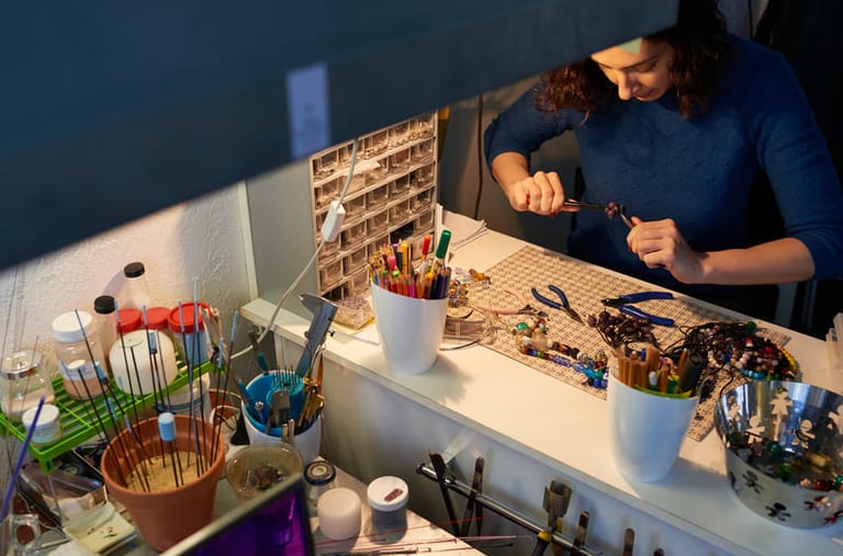 Fabricante de joyería utilizando pinzas para elaborar collares artesanales en un banco.