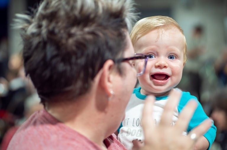 Camera focused on a smiling baby held by an adult