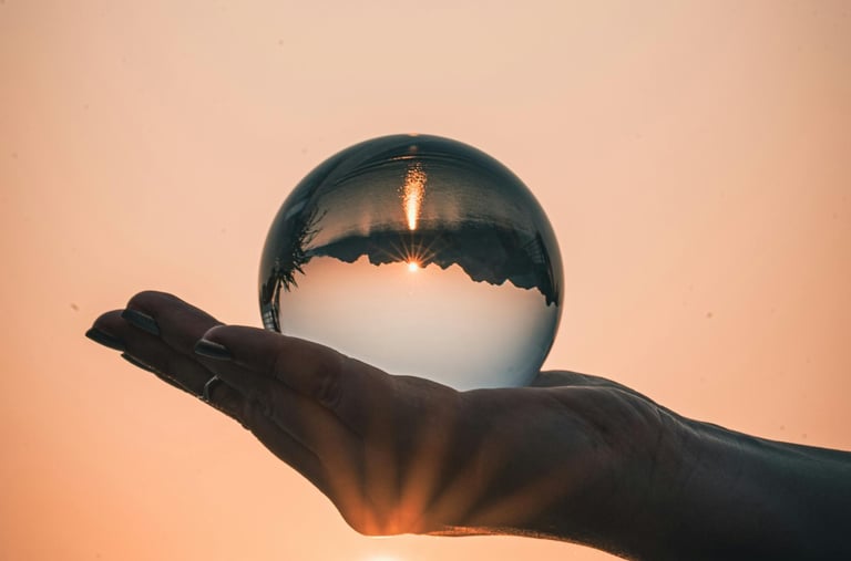 Hand holding a crystal ball reflecting a golden sunset over mountain peaks and lake water.
