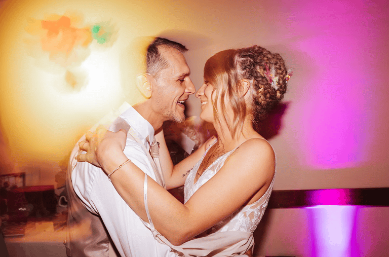 Les mariés dansent et sourient sous les lumières colorées pendant la soirée.