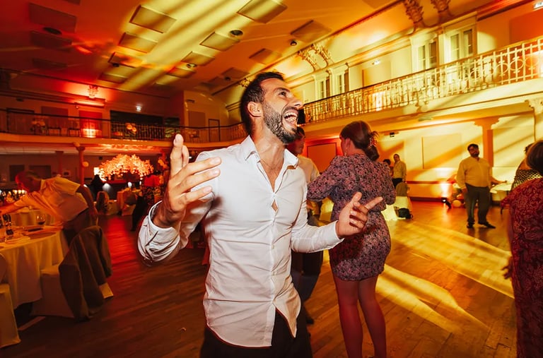Un invité en chemise blanche, les bras levés et le sourire éclatant, profite pleinement.