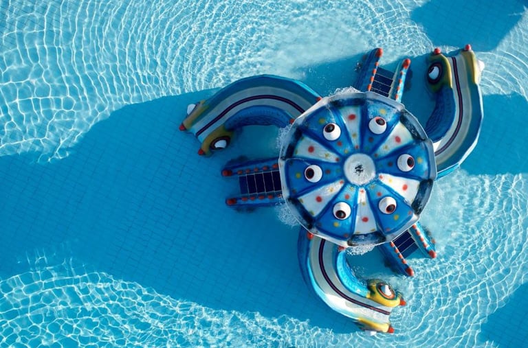 Aerial view of a colorful octopus-themed water slide in a clear blue resort swimming pool.
