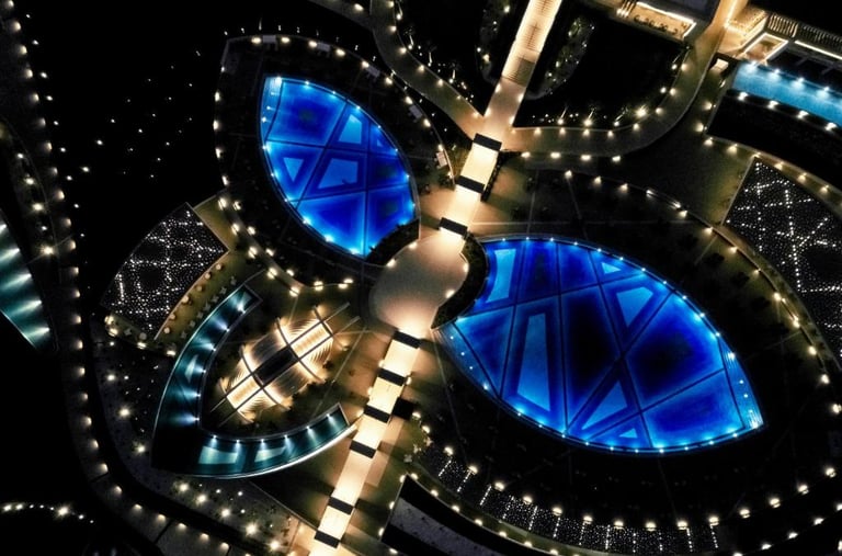 Aerial night view of a luxury resort with illuminated blue swimming pools and geometric walkways.