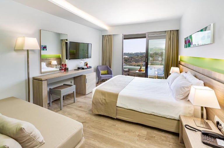 Modern hotel room with king bed, desk, wall-mounted TV, and private balcony with a scenic view.