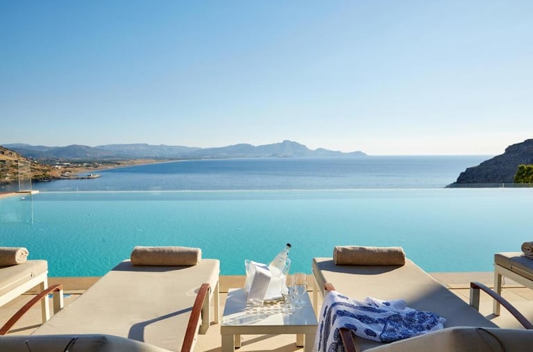 Luxury infinity pool overlooking the Mediterranean Sea with sun loungers at a tropical resort.