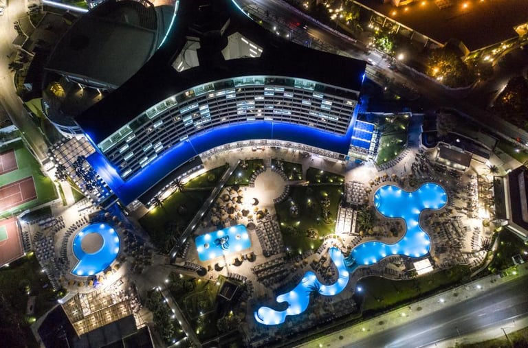Aerial night view of a luxury resort with illuminated swimming pools and modern architecture.