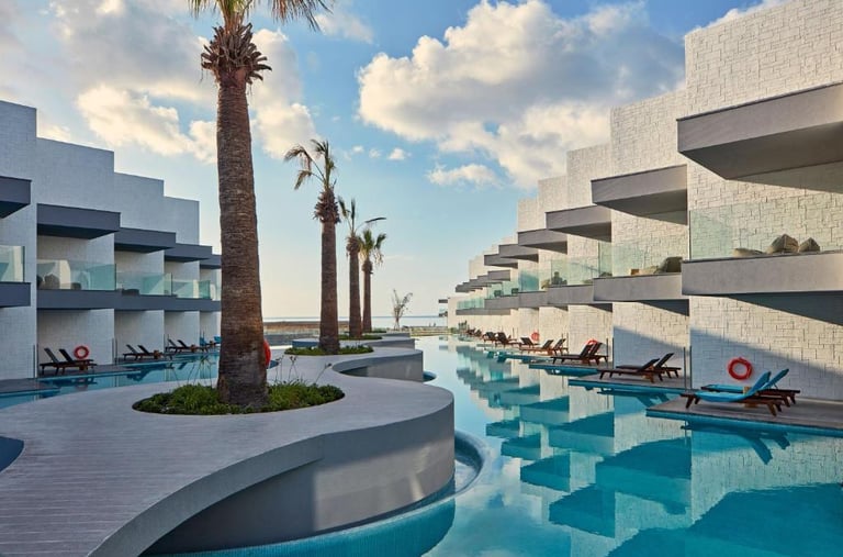 Luxury modern beachfront resort with swim-up suites, infinity pool, and palm trees under a blue sky.