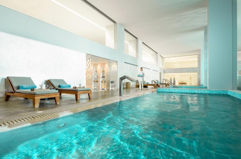 Luxury indoor spa pool with turquoise mosaic tiles, wooden lounge chairs, and a relaxation area.