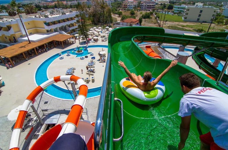 A girl on an inflatable ring slides down a green water slide at a sunny summer resort waterpark.