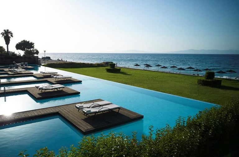 Luxury infinity pool with wooden sun decks and lounge chairs overlooking a beach and ocean.