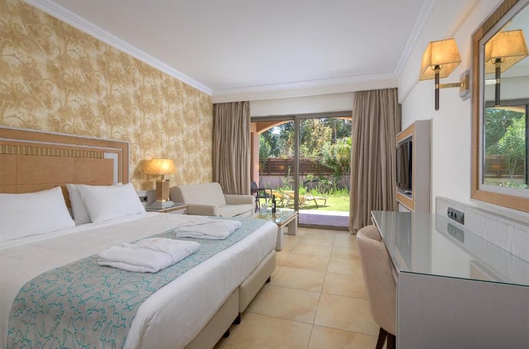 Luxury hotel room with a double bed, patterned wallpaper, and glass doors leading to a private garden patio.