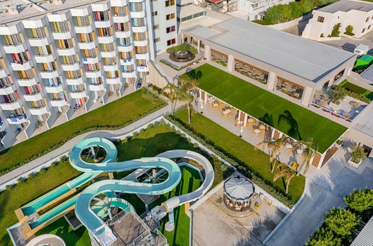 Aerial view of a luxury family resort featuring a large hotel building, outdoor water slides, and a rooftop garden.