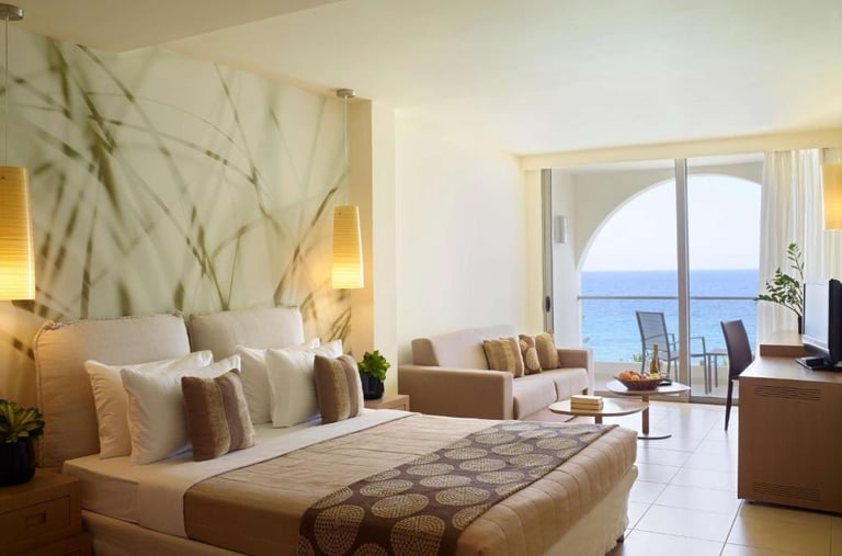 Luxury beachfront hotel room with king bed, lounge seating, and private balcony overlooking the ocean.