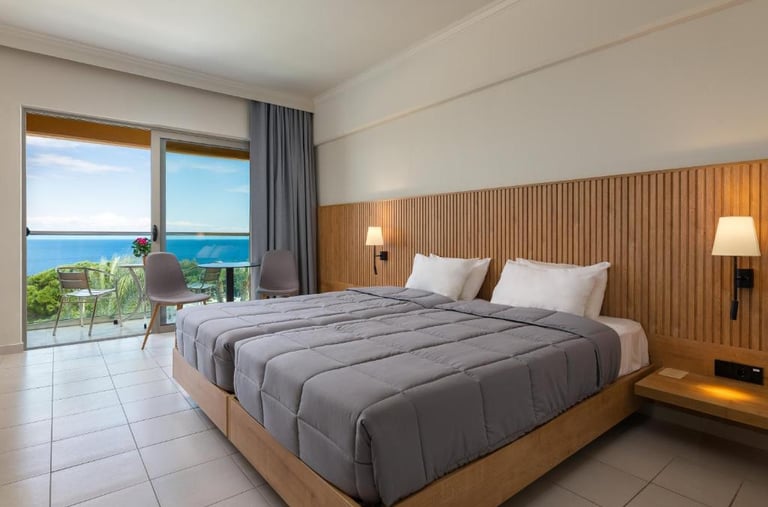 Modern hotel room with twin beds, wood paneling, and a private balcony overlooking the blue ocean.