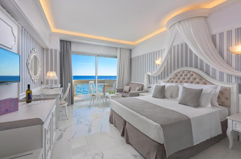 Luxury hotel room with a sea view balcony, marble floors, and elegant canopy bed.