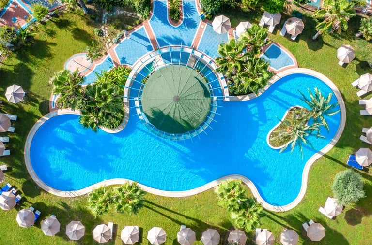 Aerial view of a Atrium Palace swimming pool with palm trees, sun loungers, and blue water.