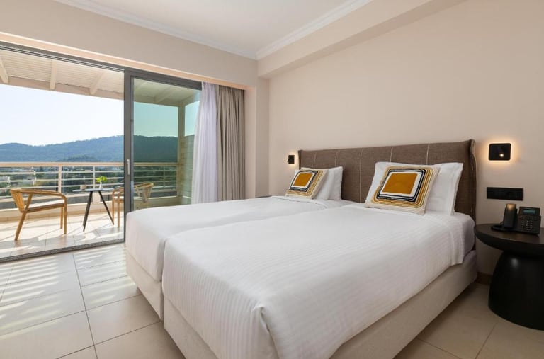 Modern hotel room with twin beds and a private balcony overlooking scenic mountains.