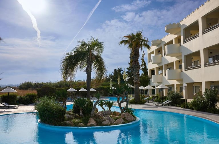 Luxury tropical resort swimming pool with palm trees and hotel balcony views under a sunny sky.