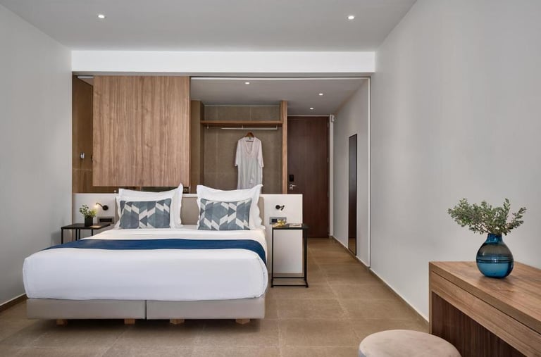 Modern hotel suite with a king-sized bed, white linens, blue accents, and a contemporary wood desk.