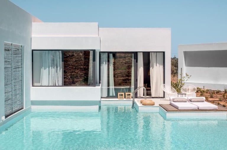 Modern luxury villa with a private turquoise swimming pool and sun loungers under a clear sky.