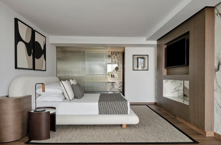 Modern luxury hotel bedroom with a minimalist white bed, wooden wall paneling, and an ensuite marble bathroom.