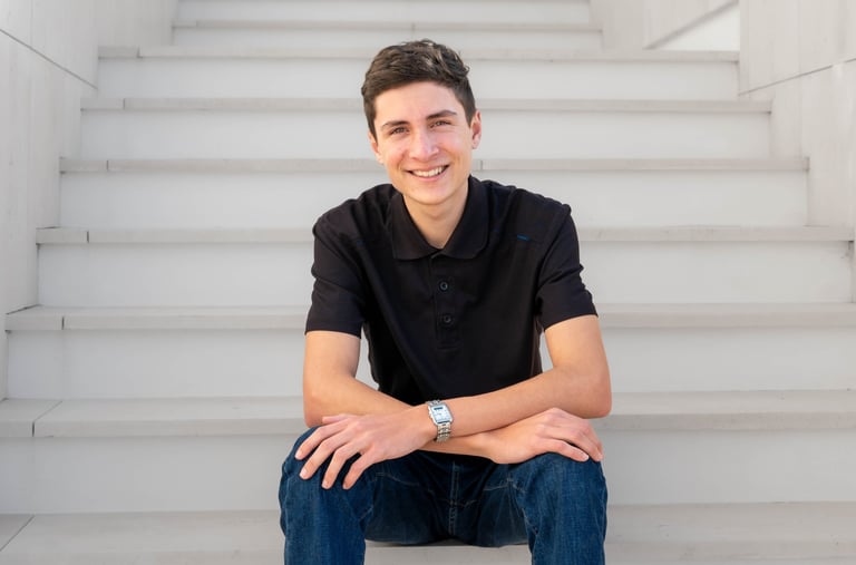 A stylish, confident young entrepreneur poses on stairs with direct eye contact and a welcoming smile.