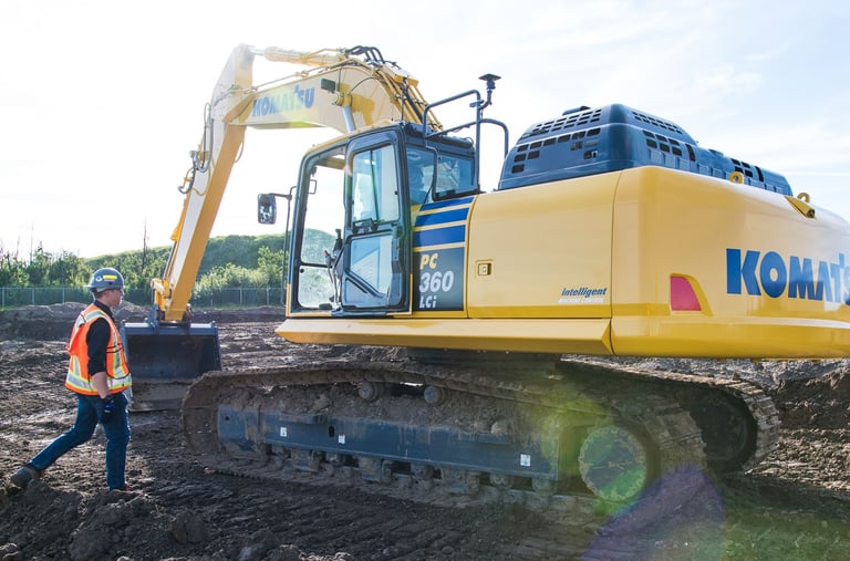 A heavy equipment technician is seen approaching a Komatsu PC360LCi smart construction excavator.