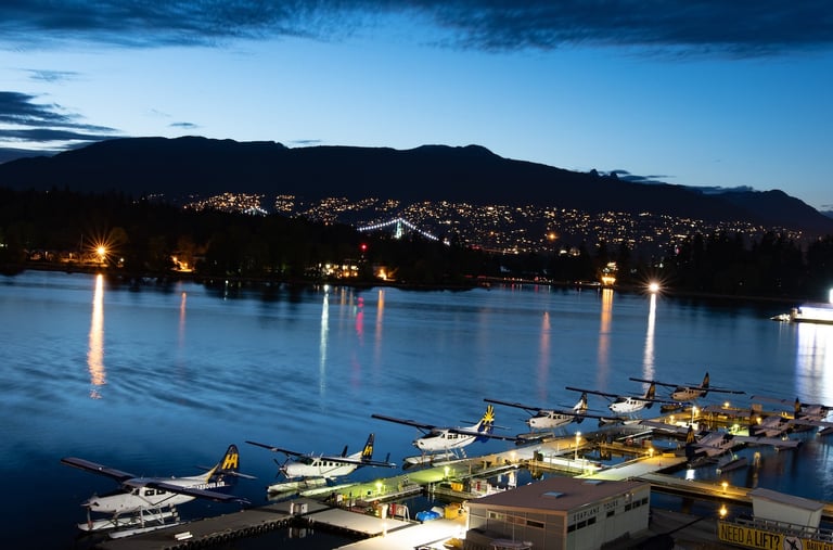 Harbour Air float aircraft lined up at Vancouver's dock at night, with Stanley Park and the Lions Gate bridge illuminated.