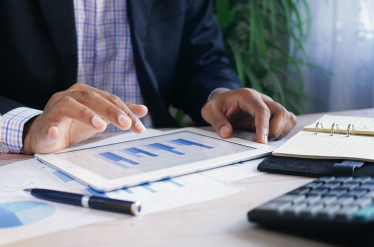 Hands of person of color at a desk looking at bar graphs on a tablet