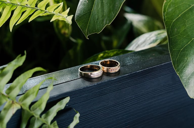 Fotografía premium de detalle de anillos de bodas reodeados de plantas en un fondo de madera azul en Quito