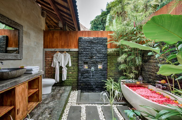 Luxury outdoor bathroom in Bali featuring a stone shower and a bathtub filled with red flower petals.