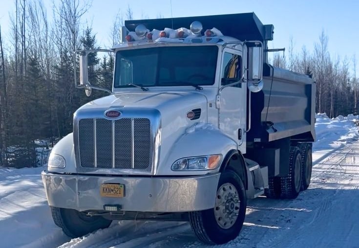 White Peterbilt dump truck parked on a snowy winter road with forest background.