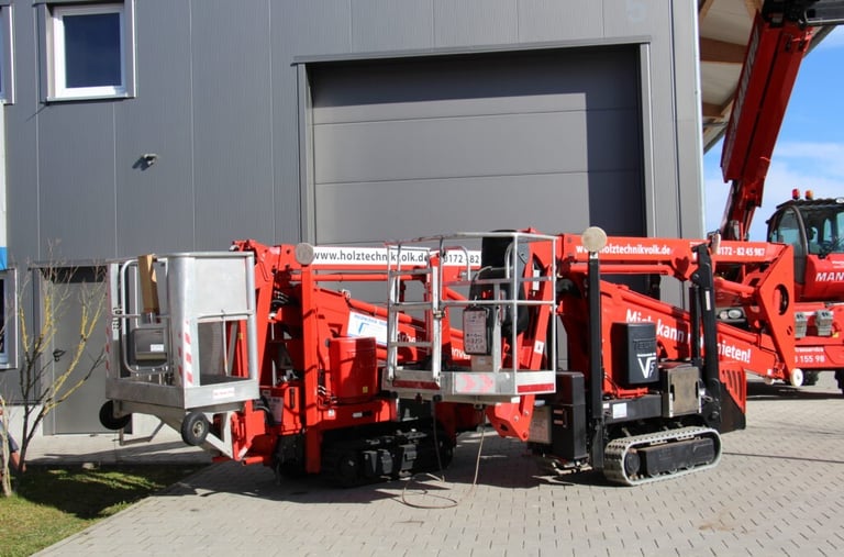 Zwei rote Raupen-Arbeitsbühnen mit silbernen Körben stehen nebeneinander vor einer grauen Industriehalle der Schreinerei Volk