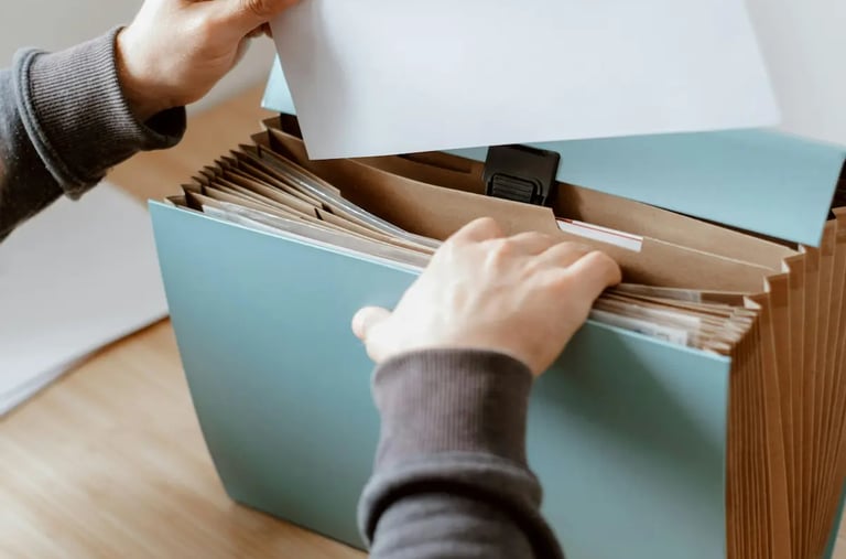 A person organizing documents in a blue accordion expanding file folder on a wooden desk.