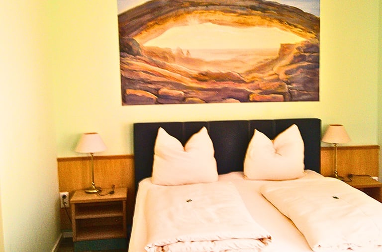 Cozy hotel room with double bed, bedside lamps, and a scenic canyon landscape painting above the headboard.