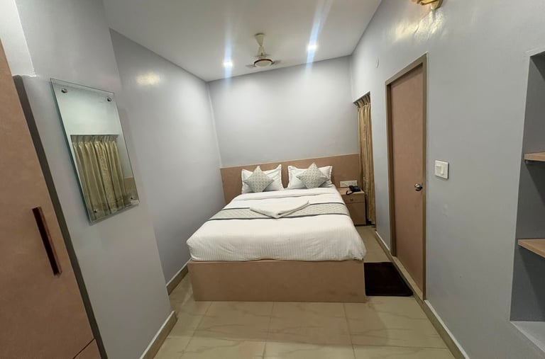 Modern minimalist hotel bedroom with a white double bed, wood headboard, and wall-mounted mirror.