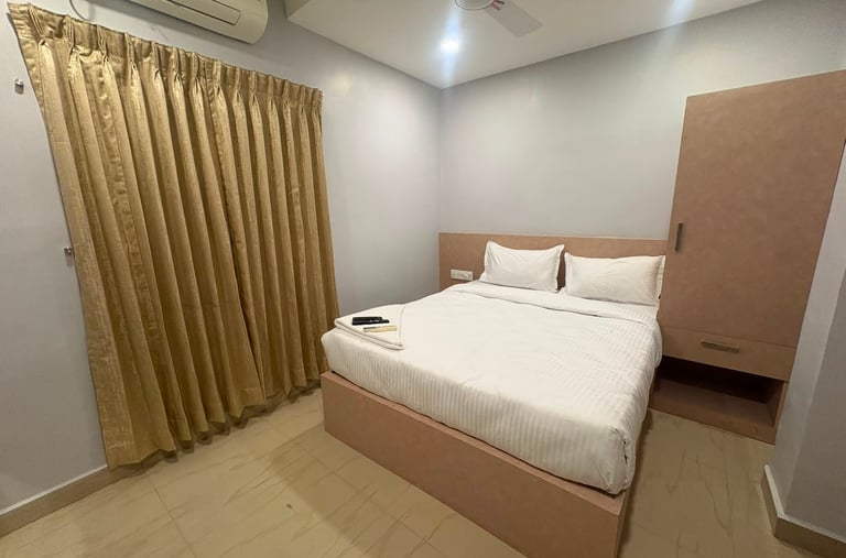 Modern minimalist hotel bedroom with white linens, gold curtains, and a wooden wardrobe cabinet.