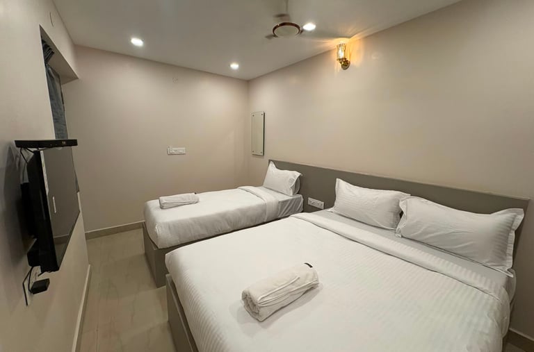 Modern hotel room featuring a twin bed and queen bed with white linens and a wall-mounted TV.