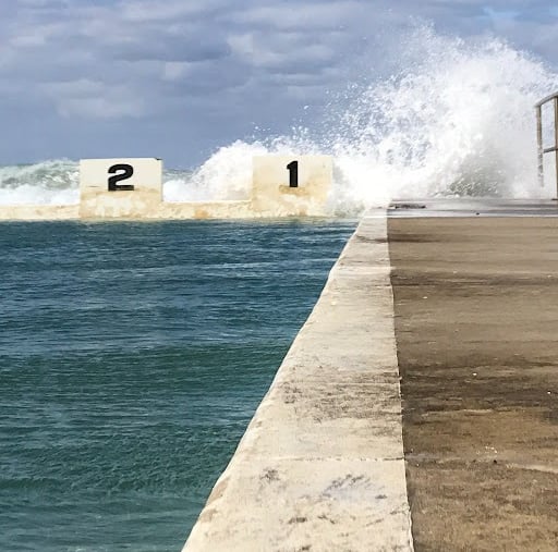 Ocean swimming pool with wave splashing over swim lane starting blocks numbered 1 and 2