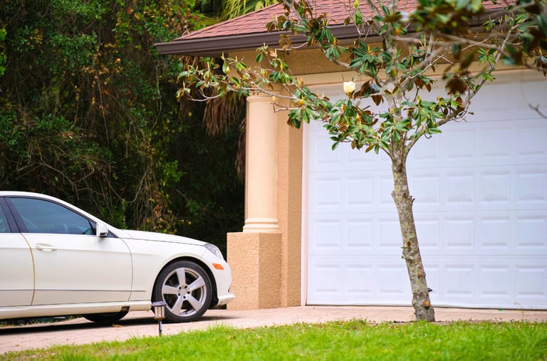 White sedan parkedo on a paved driveway in front of a modern home with a white sectional garage dor.