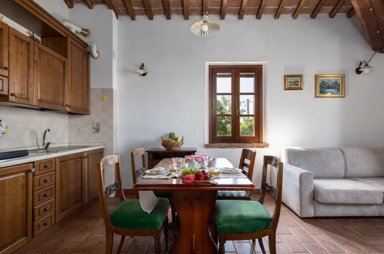 Rustic open plan kitchen and dining area with wooden table, green chairs, and exposed ceiling beams.