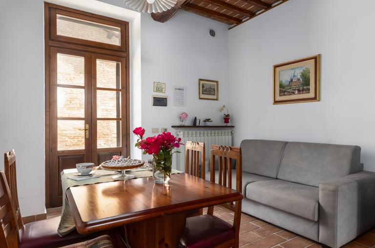 Rustic Italian dining room with a wooden table, gray sofa, and balcony doors.