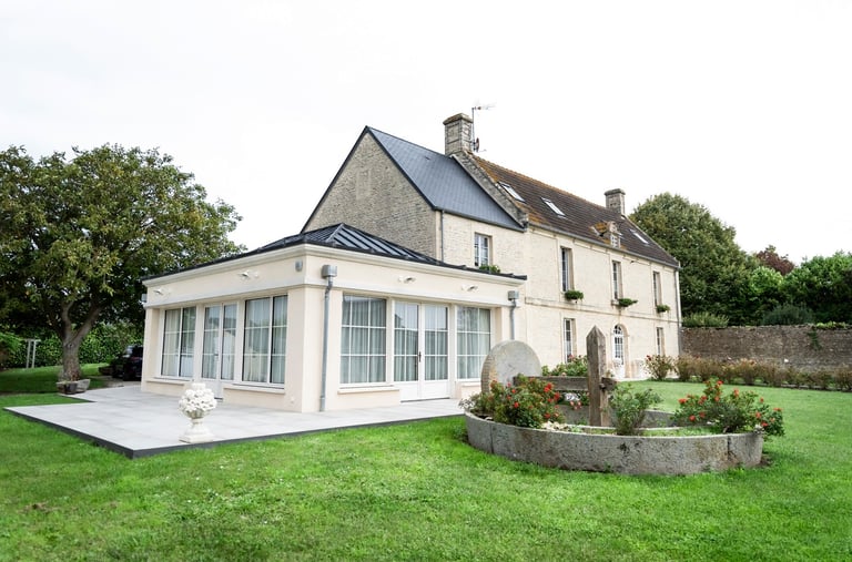Maison en campagne avec une façade en pierre, entourée d'un jardin verdoyant et de grands arbres.