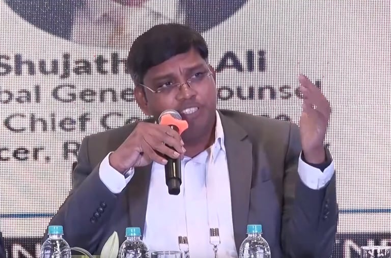 a man in a suit and glasses speaking into a microphone